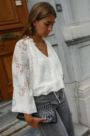 Blouse en dentelle col V portée par une femme, vue de trois-quarts, pochette à la main, jean gris