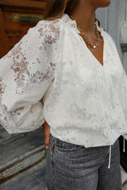 Blouse en dentelle col V portée par une femme, gros plan des manches en dentelle et du jean gris