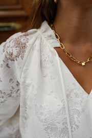 Blouse en dentelle col V portée par une femme, gros plan du col V et de la dentelle, collier doré