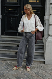 Blouse en dentelle col V portée par une femme, silhouette entière, jean gris, sac bordeaux, escaliers