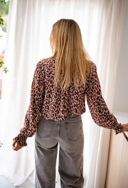Blouse imprimée fluide portée par une femme, vue de dos, rideaux blancs, jean gris