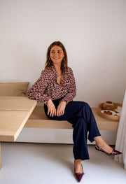 Blouse imprimée fluide portée par une femme, assise, banquette en bois, escarpins