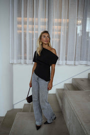Blouse à épaule dénudée noire portée par une femme, vue de trois-quarts, escalier, sac à main bordeaux