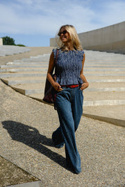 Blouse froncée sans manches portée par une femme, silhouette entière, sur des gradins, sac sur l'épaule