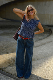 Blouse froncée sans manches portée par une femme, vue de trois-quarts, main dans les cheveux, sac bordeaux