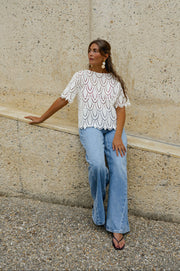 Blouse crochet manches courtes portée par une femme, vue de trois-quarts, adossée à un mur