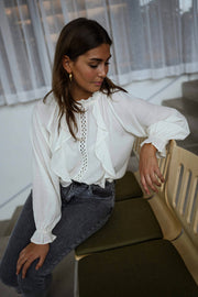 Blouse brodée à col montant écrue portée par une femme, assise, banc kaki, jean gris