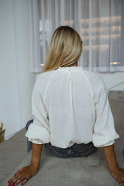 Blouse brodée à col montant écrue portée par une femme, vue de dos, escalier, volants