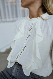 Blouse brodée à col montant écrue portée par une femme, vue rapprochée, volant brodé, jean gris