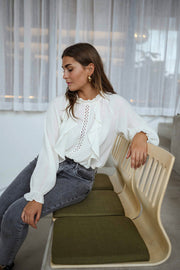 Blouse brodée à col montant écrue portée par une femme, assise, banc kaki, main sur le dossier