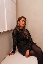 Blouse transparente à col plissé noire portée par une femme, assise, assise sur un banc, mains sur les genoux