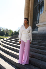 Blouse cache-cœur fluide portée par une femme, silhouette entière, pantalon rose, sur des escaliers