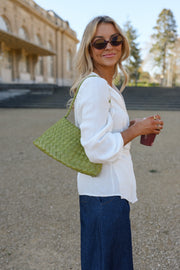 Blouse cache-cœur fluide portée par une femme, silhouette entière, lunettes de soleil, sac vert à la main