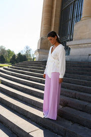 Blouse cache-cœur fluide portée par une femme, vue de profil, pantalon rose, sur des escaliers