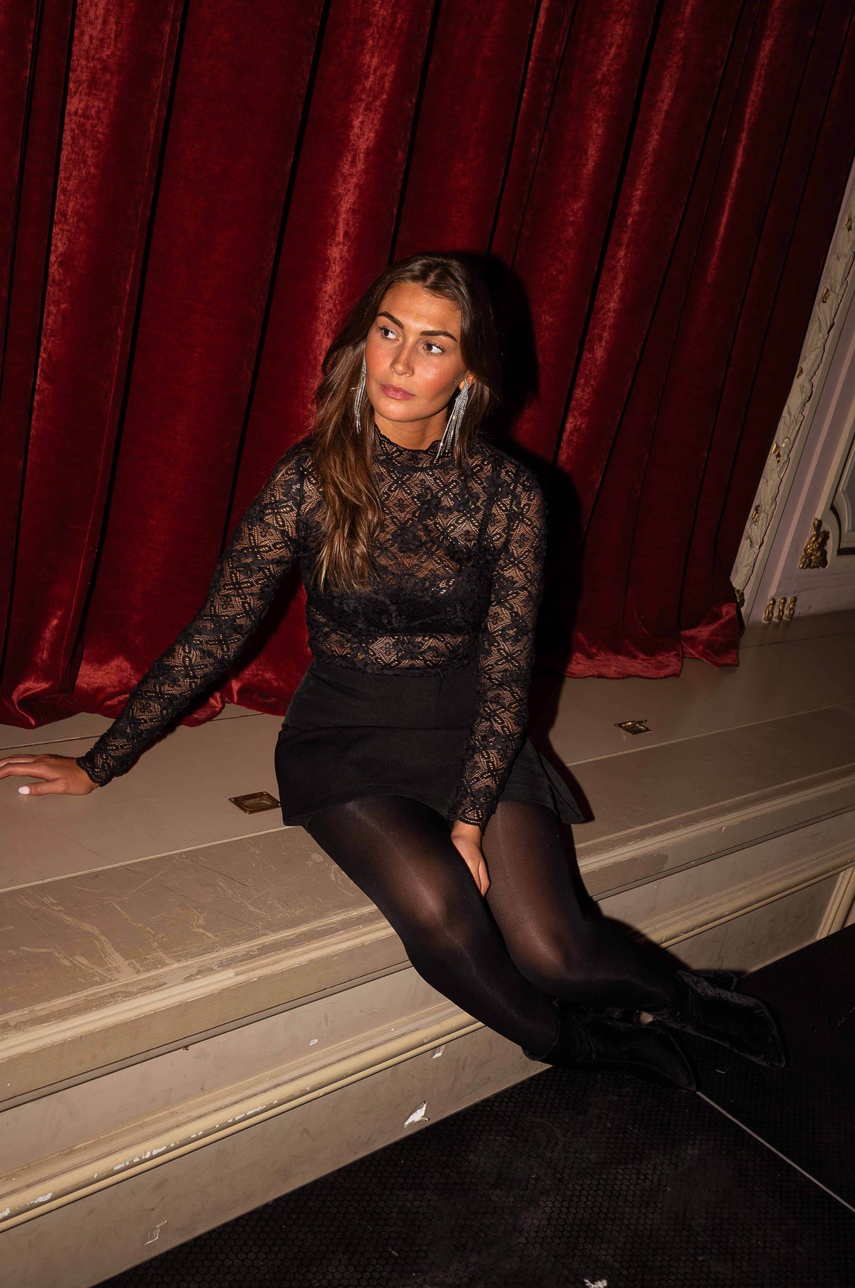 Blouse en dentelle transparente noire portée par une femme, assise, assise, dentelle, rideau rouge