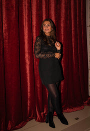 Blouse en dentelle transparente noire portée par une femme, silhouette entière, rideau rouge, collants noirs