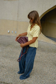 Blouse cintrée boutonnée manches courtes portée par une femme, vue de trois-quarts, vêtement bordeaux sur le bras