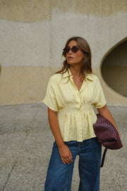 Blouse cintrée boutonnée manches courtes portée par une femme, vue rapprochée, lunettes de soleil, vêtement bordeaux sur le bras