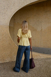 Blouse cintrée boutonnée manches courtes portée par une femme, vue de dos, sac bordeaux à la main