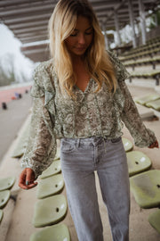 Blouse volantée à col V portée par une femme, vue de face, gradins verts, jean gris