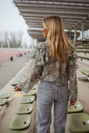 Blouse volantée à col V portée par une femme, vue de trois-quarts, gradins verts, cheveux blonds