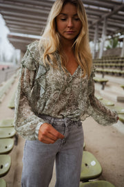 Blouse volantée à col V portée par une femme, vue de face, gradins, main dans la poche