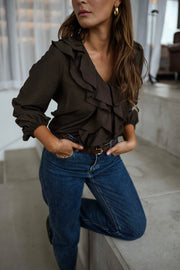 Blouse fluide à volants chocolat portée par une femme, vue de face, rideaux blancs, jean bleu