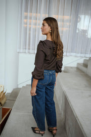 Blouse fluide à volants chocolat portée par une femme, vue de profil, rideaux blancs, queue-de-cheval