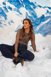 Blouse léopard légèrement transparente portée par une femme, assise, assise au sol, jean foncé