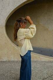 Blouse douce ample boutonnée portée par une femme, vue de trois-quarts, devant un mur courbe, main dans les cheveux