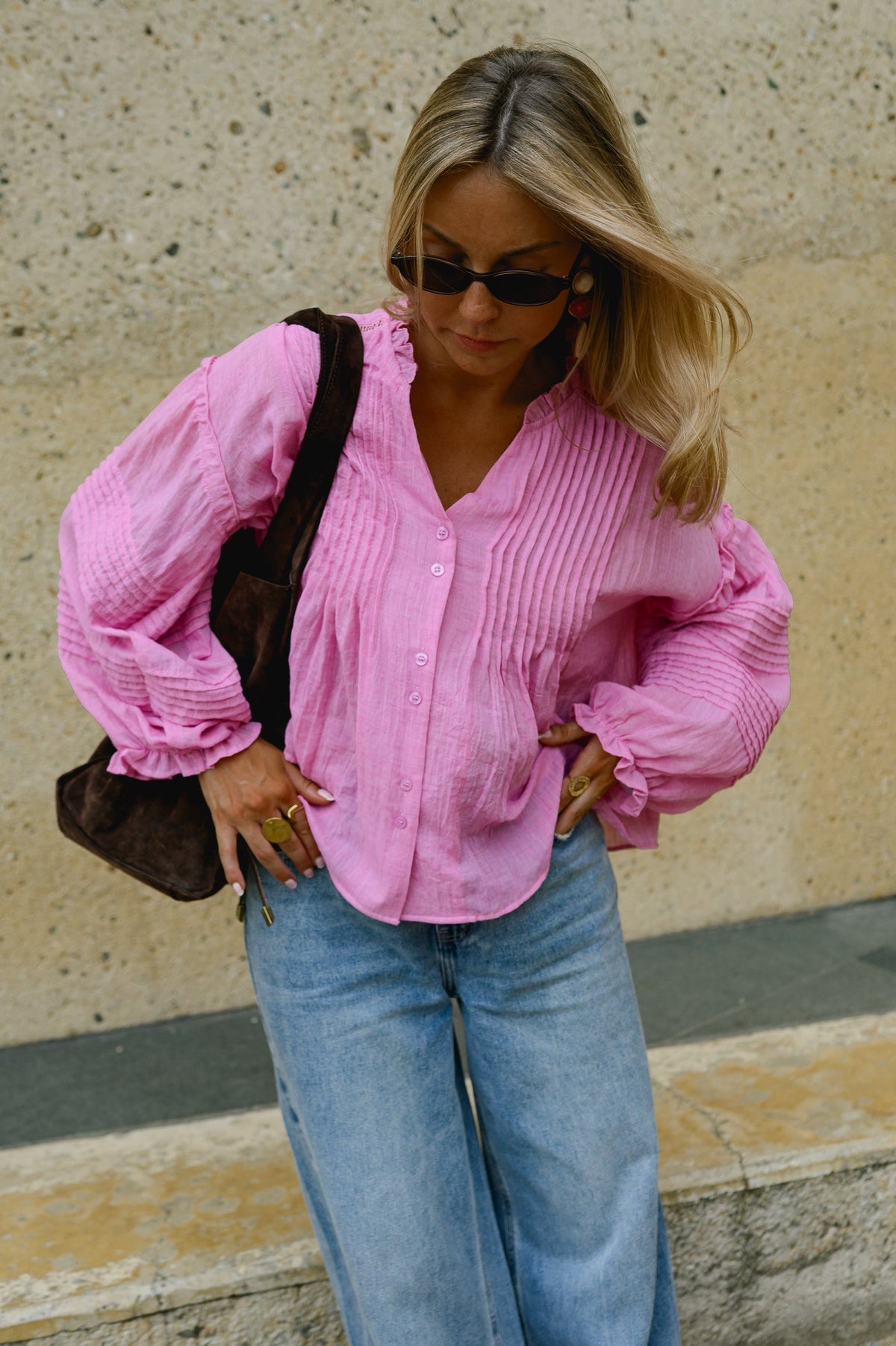 Blouse boutonnée à manches évasées portée par une femme, vue rapprochée, lunettes de soleil, sac à l'épaule