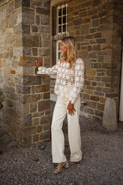 Blouse brodée à manches évasées écrue portée par une femme, vue de face, mur en pierre, fenêtre