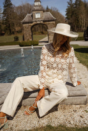 Blouse brodée à manches évasées écrue portée par une femme, assise, chapeau blanc, bord du bassin