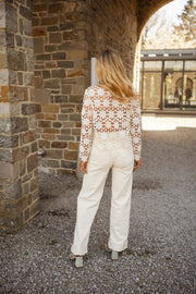 Blouse brodée à manches évasées écrue portée par une femme, vue de dos, arche en pierre, pantalon blanc