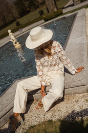 Blouse brodée à manches évasées écrue portée par une femme, assise, chapeau blanc, bassin