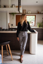 Blouse gaufrée à boutons noire portée par une femme, silhouette entière, cuisine, tabouret