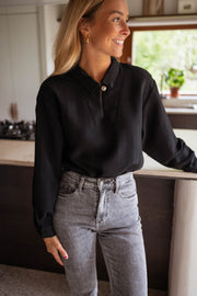 Blouse gaufrée à boutons noire portée par une femme, vue de face, cuisine, jean gris