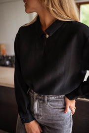 Blouse gaufrée à boutons noire portée par une femme, vue rapprochée, manches, jean