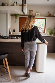 Blouse gaufrée à boutons noire portée par une femme, vue de dos, cuisine, tabouret