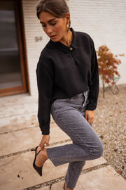 Blouse gaufrée à boutons noire portée par une femme, vue de profil, allée dallée, jean gris