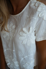 Blouse brodée à manches courtes écrue portée par une femme, vue rapprochée, fleurs brodées, encolure