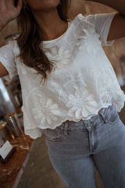 Blouse brodée à manches courtes écrue portée par une femme, vue rapprochée, fleurs brodées, jean clair