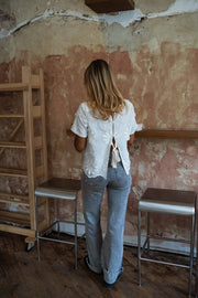 Blouse brodée à manches courtes écrue portée par une femme, vue de dos, mur patiné, jean clair
