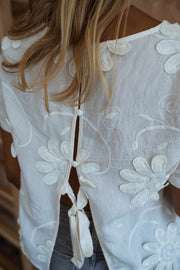 Blouse brodée à manches courtes écrue portée par une femme, vue rapprochée, lacet dans le dos, fleurs brodées