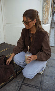 Blouse brodée à boutons chocolat portée par une femme, assise, sol, lunettes de soleil, gobelet