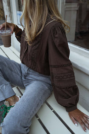 Blouse brodée à boutons chocolat portée par une femme, vue de profil, banc blanc, jean clair
