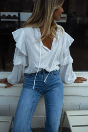 Blouse plumetis à volants écrue portée par une femme, vue de face, banc blanc, jean bleu