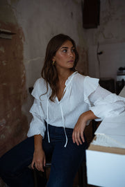 Blouse plumetis à volants écrue portée par une femme, vue de trois-quarts, mur patiné, regard de côté
