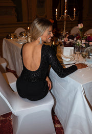 Body pailleté à dos ouvert porté par une femme, assise, assise sur la table, cheveux attachés
