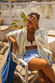 Chemise rayée en gaze portée par une femme, assise, chaise, sac cabas bleu